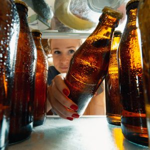 View from inside the refrigerator of a woman putting bottle of beer in the refrigerator.